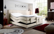 Boxspringbett in modernem Schlafzimmer, seitliche Perspektive, mit verstellbaren Matratzen und hellem Stoffbezug.