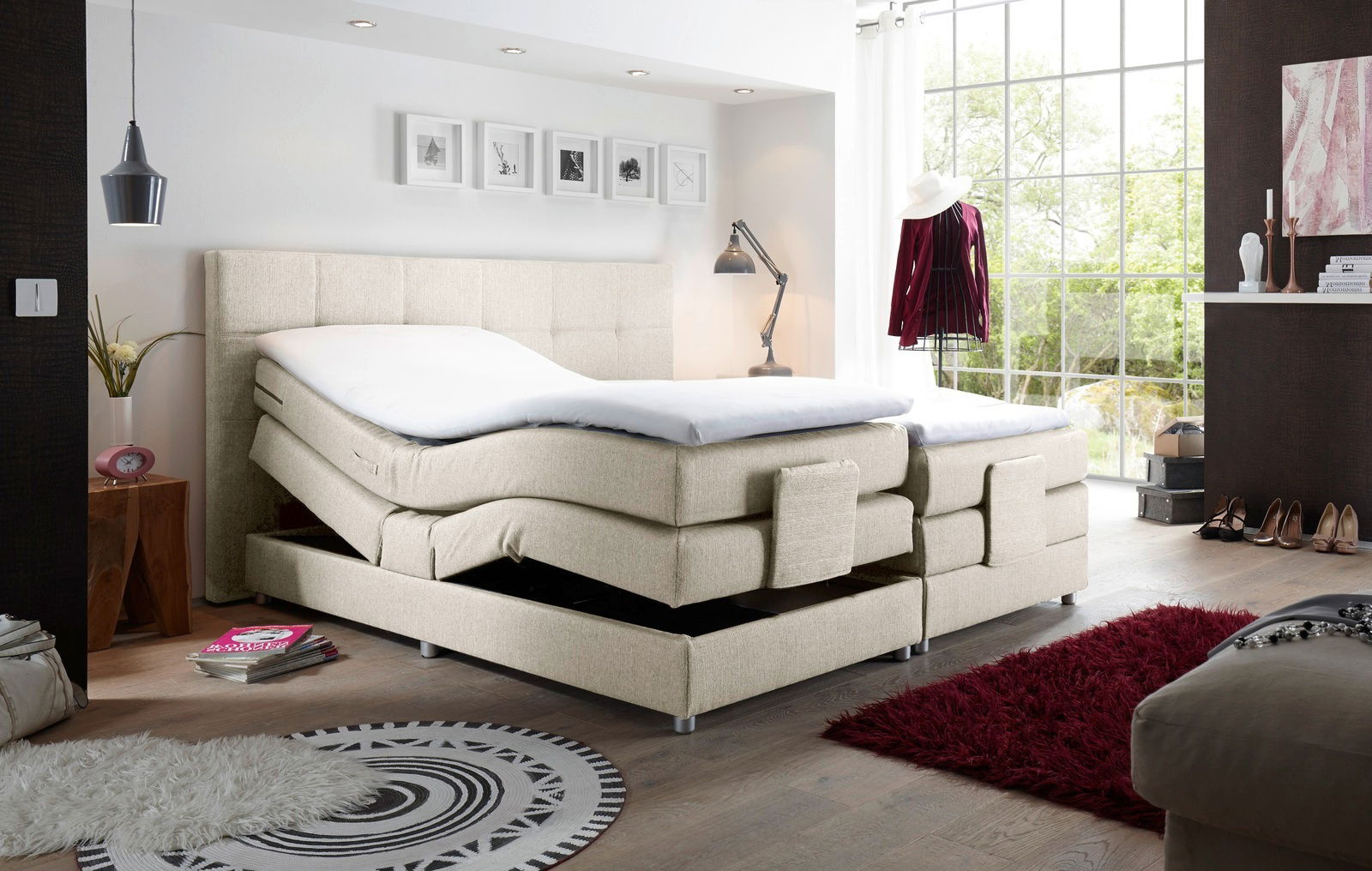 Boxspringbett in modernem Schlafzimmer, seitliche Perspektive, mit verstellbaren Matratzen und hellem Stoffbezug.