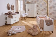 Gemütliches Babyzimmer mit Wickelkommode, Kleiderschrank, Gitterbett und Plüschbär, aus der Perspektive eines Betrachters im Raum.