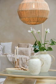 Ein stilvoller Kerzenständer aus Holz mit brennenden Kerzen, im Hintergrund gemütliche Kissen und eine dekorative Vase mit Blumen, aus der Perspektive eines Wohnzimmers.