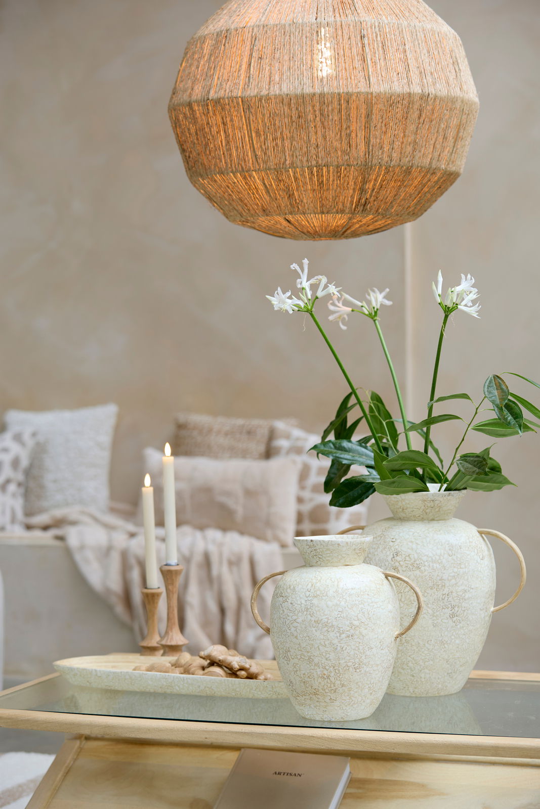Ein stilvoller Kerzenständer aus Holz mit brennenden Kerzen, im Hintergrund gemütliche Kissen und eine dekorative Vase mit Blumen, aus der Perspektive eines Wohnzimmers.