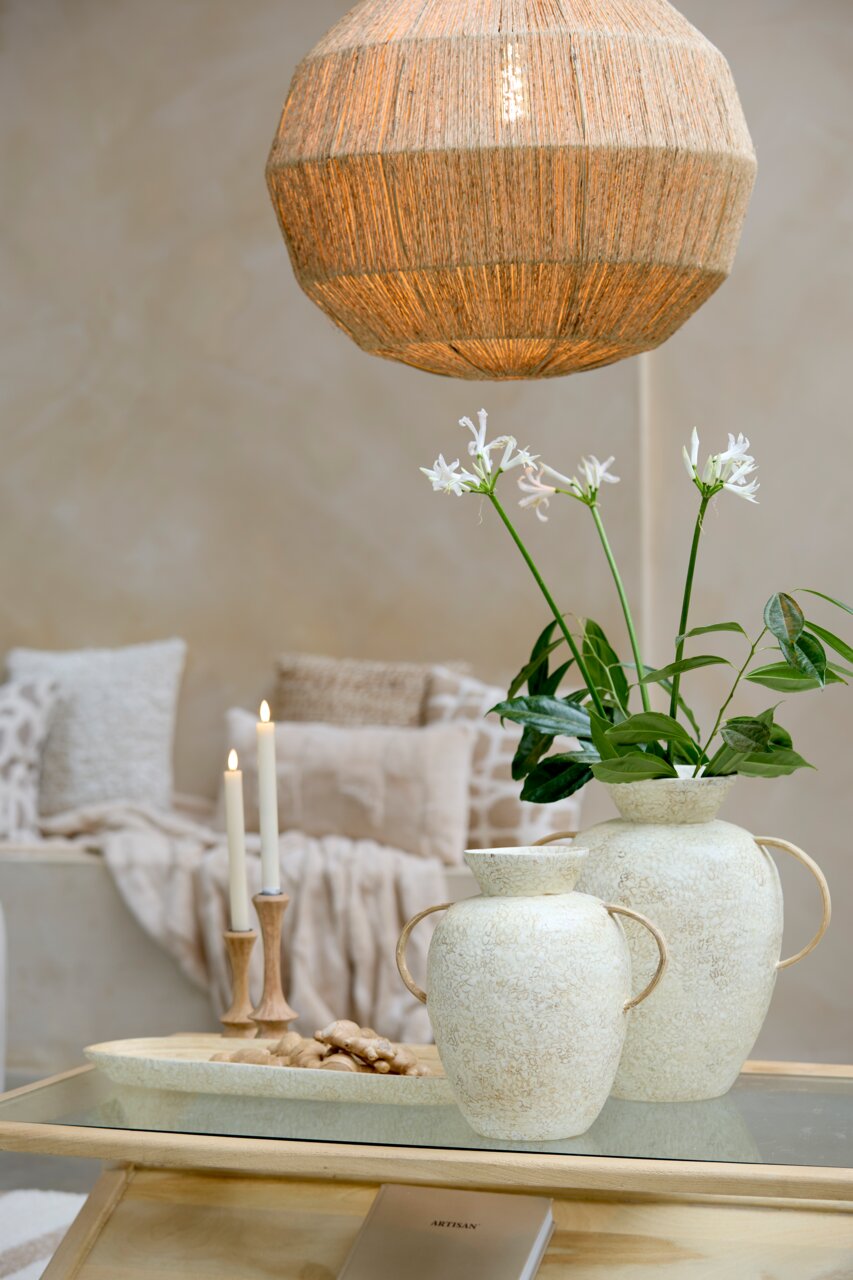 Ein stilvoller Kerzenständer aus Holz mit brennenden Kerzen, im Hintergrund gemütliche Kissen und eine dekorative Vase mit Blumen, aus der Perspektive eines Wohnzimmers.