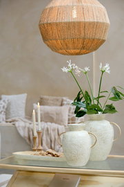 Ein stilvoller Kerzenständer aus Holz mit brennenden Kerzen, im Hintergrund gemütliche Kissen und eine dekorative Vase mit Blumen, aus der Perspektive eines Wohnzimmers.