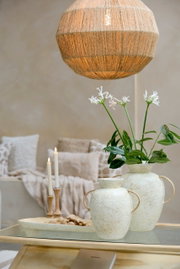 Ein stilvoller Kerzenständer aus Holz mit brennenden Kerzen, im Hintergrund gemütliche Kissen und eine dekorative Vase mit Blumen, aus der Perspektive eines Wohnzimmers.