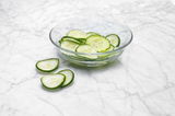 Schale mit frisch geschnittenen Gurkenscheiben auf einer Marmoroberfläche, seitliche Perspektive
