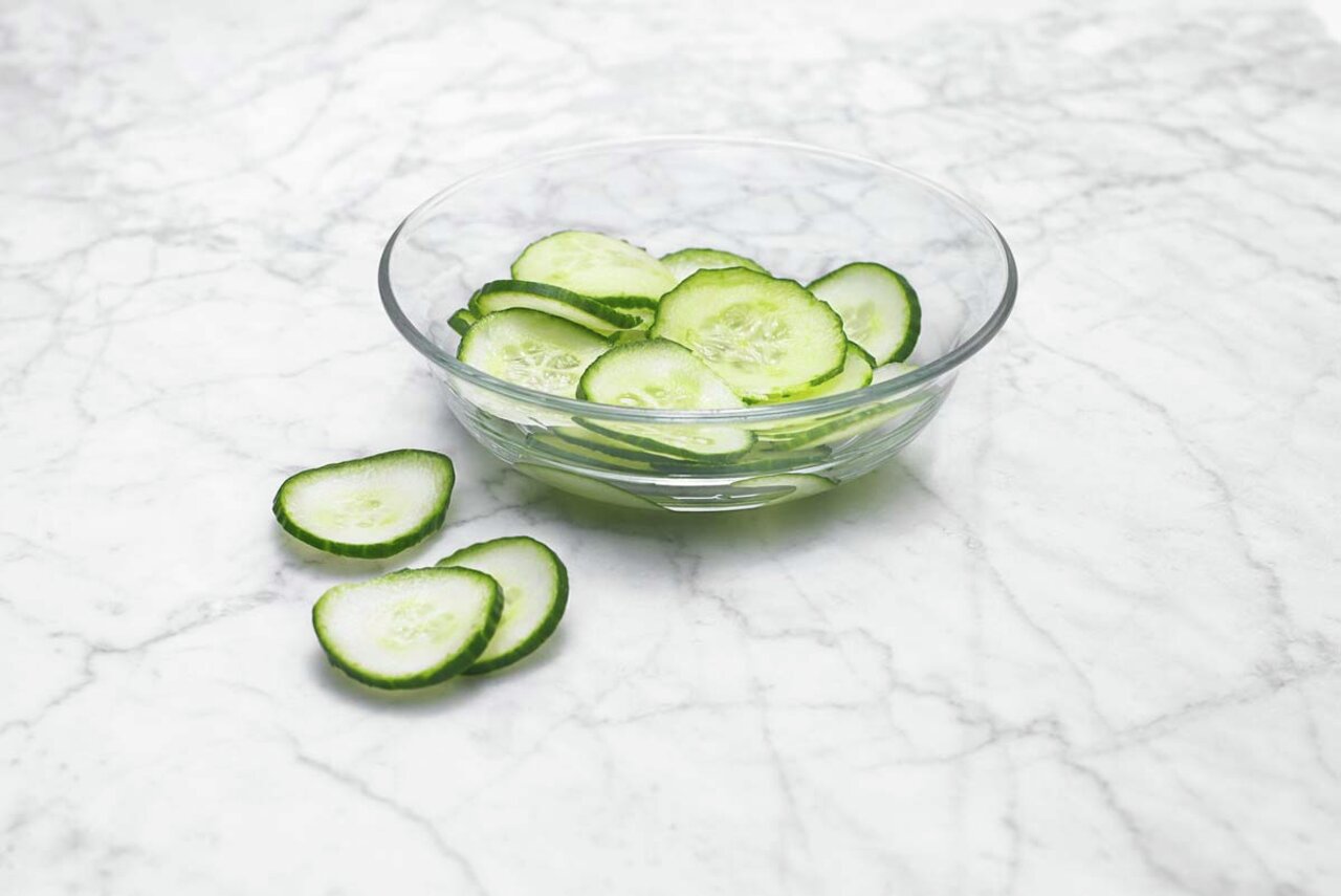 Schale mit frisch geschnittenen Gurkenscheiben auf einer Marmoroberfläche, seitliche Perspektive