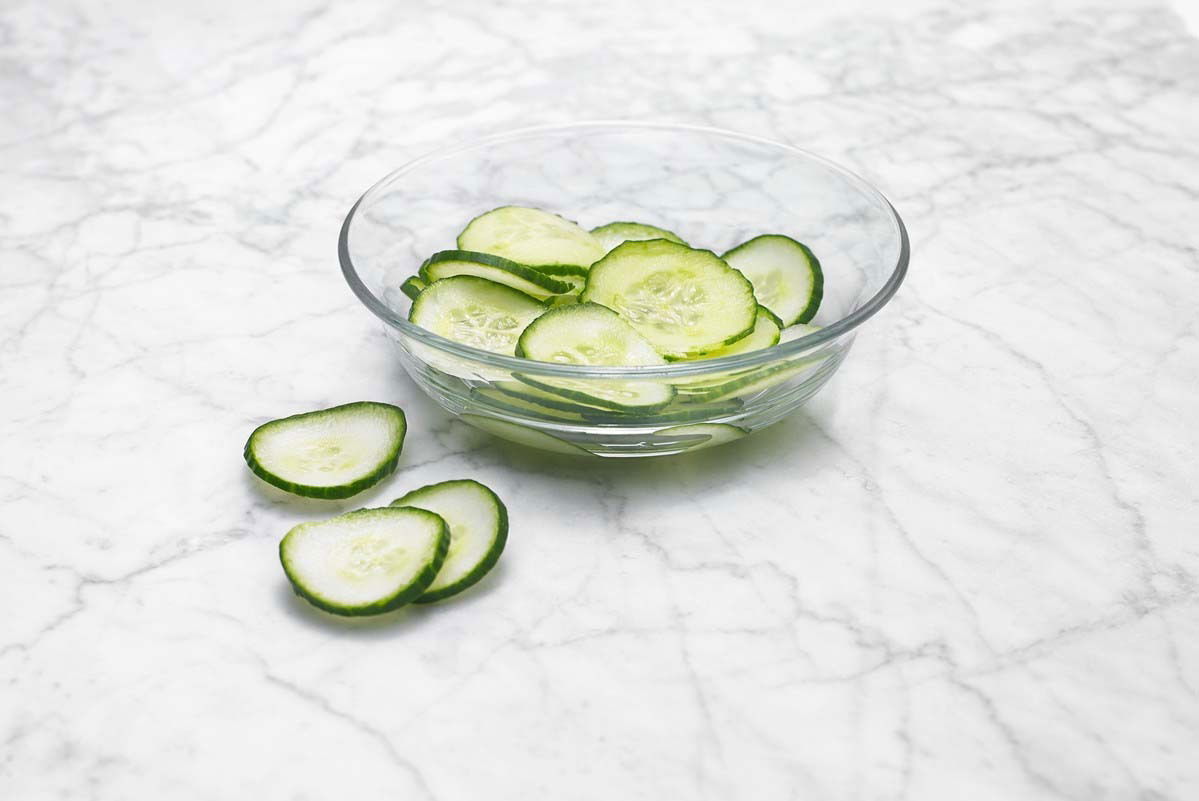 Schale mit frisch geschnittenen Gurkenscheiben auf einer Marmoroberfläche, seitliche Perspektive