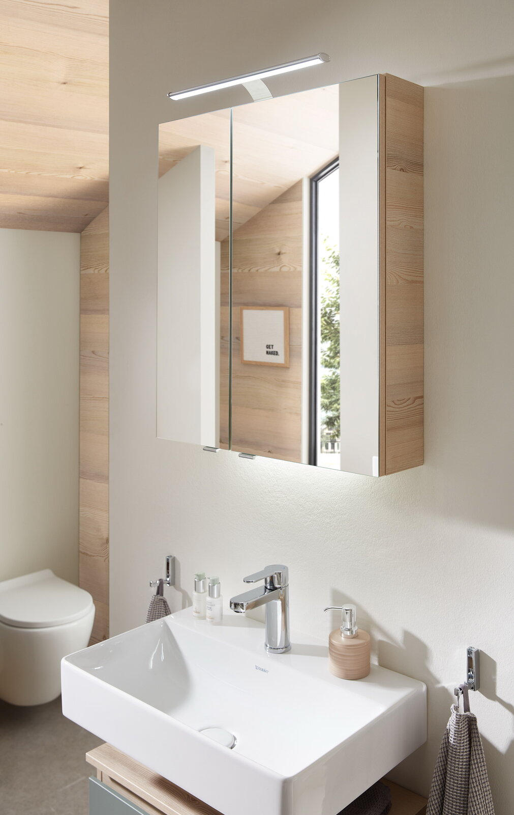Moderner Spiegelschrank mit Holzverkleidung und integrierter Beleuchtung, seitliche Perspektive im Badezimmer.