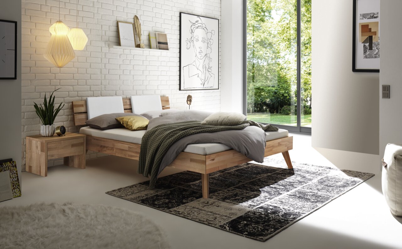 Modernes Schlafzimmer mit einem Bett aus Holz und Metall, seitliche Perspektive. Das Bett hat ein schlichtes Kopfteil und ist mit neutralen Farben dekoriert. Große Fenster lassen viel Tageslicht herein.