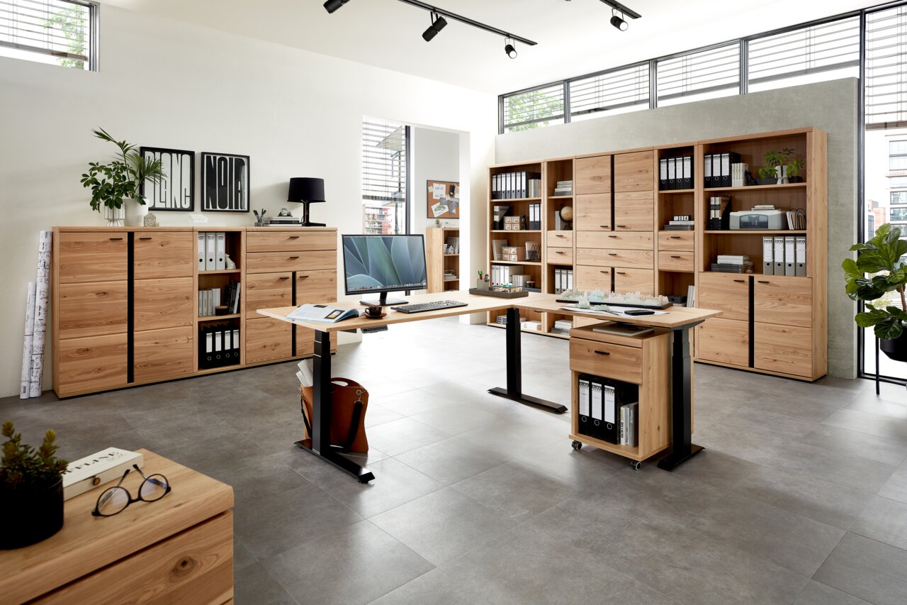 Moderne Büromöbel in einem hellen Raum mit großen Fenstern, bestehend aus einem höhenverstellbaren Schreibtisch, mehreren Aktenschränken und Regalen aus Holz. Perspektive: Frontalansicht.
