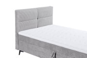 Graues Boxbett mit gestepptem Kopfteil und weißer Matratze, seitliche Perspektive