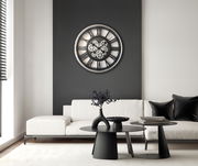 Moderne Wanduhr mit Zahnrädern in einem stilvollen Wohnzimmer, frontal an einer dunklen Wand über einem weißen Sofa montiert.