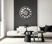 Moderne Wanduhr mit Zahnrädern in einem stilvollen Wohnzimmer, frontal an einer dunklen Wand über einem weißen Sofa montiert.