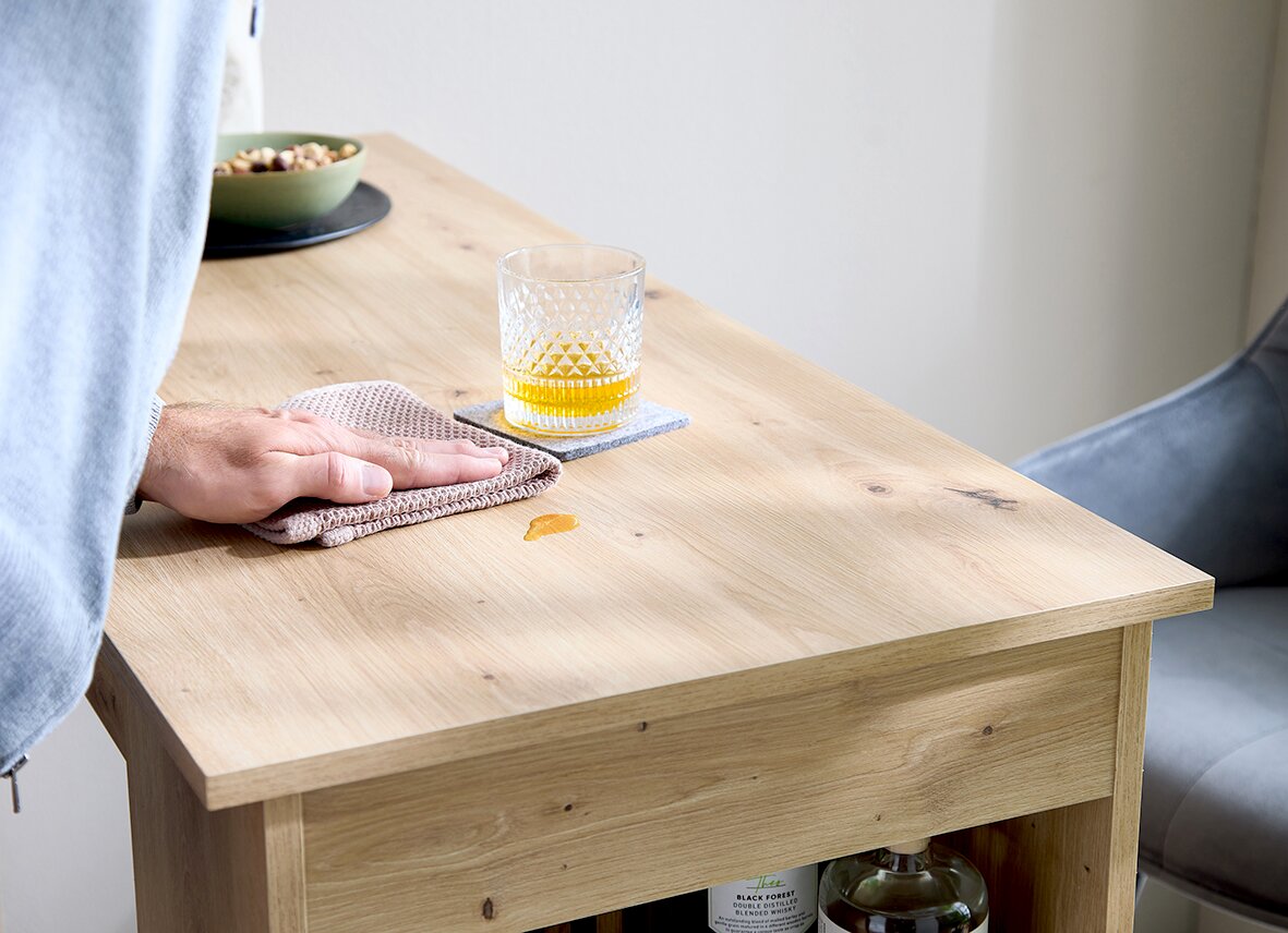 Holz-Couchtisch in heller Eichenoptik mit Glas auf Untersetzer und weggewischtem Fleck, Nahaufnahme aus leicht schräger Seitenperspektive von oben