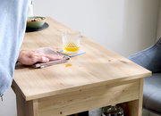 Holz-Couchtisch in heller Eichenoptik mit Glas auf Untersetzer und weggewischtem Fleck, Nahaufnahme aus leicht schräger Seitenperspektive von oben