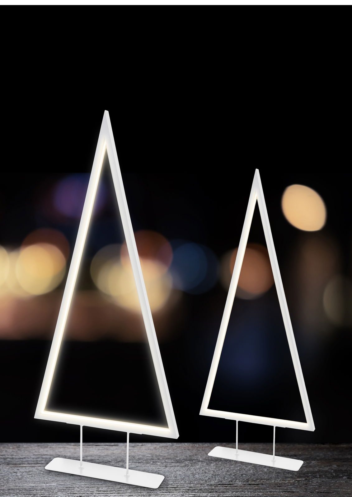 Zwei moderne LED-Bäume in Dreiecksform auf einem Tisch, mit warmem Licht vor einem unscharfen Hintergrund. Seitliche Perspektive.