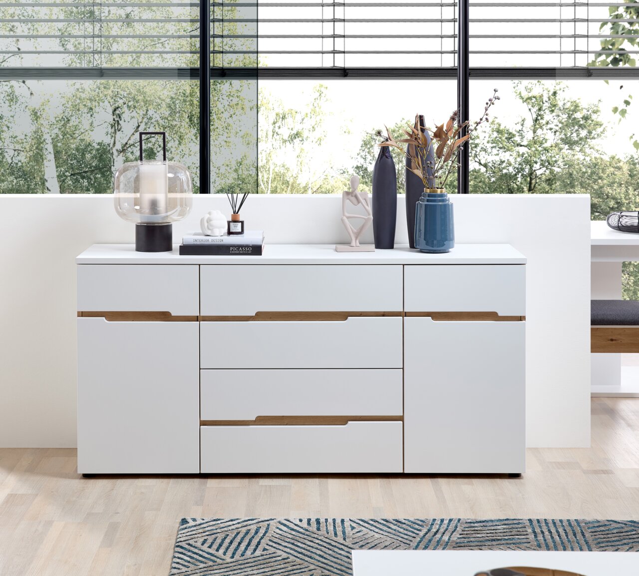 Modernes weißes Sideboard mit Holzdetails, dekoriert mit Vasen und einer Lampe, frontal fotografiert.