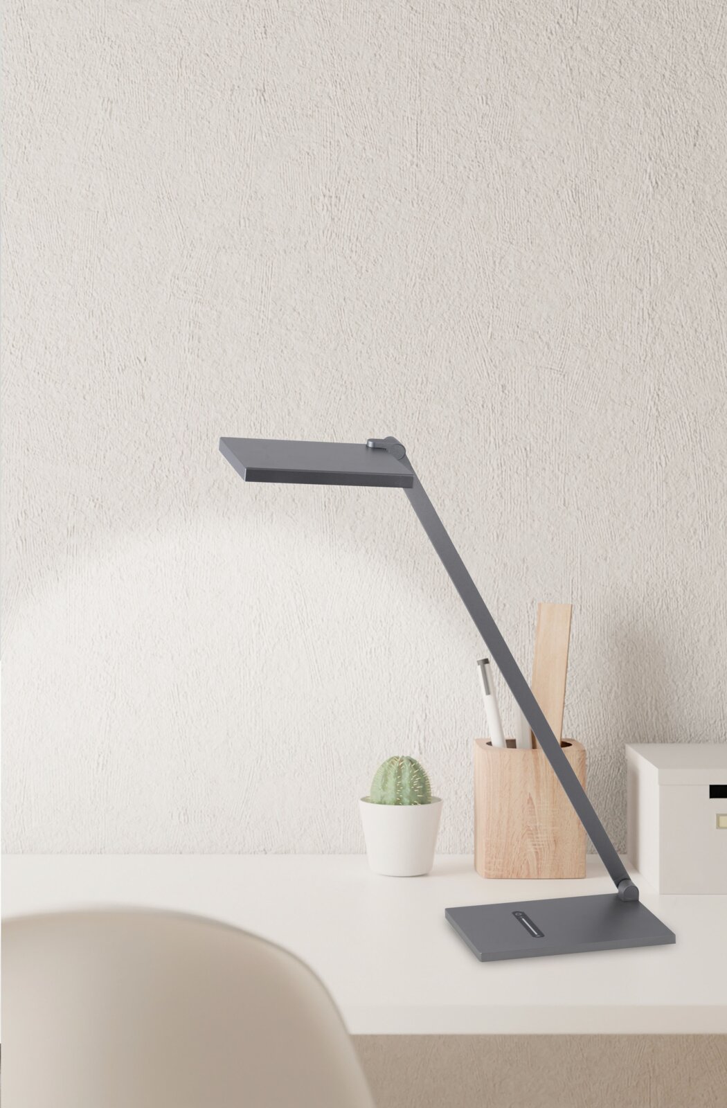 Moderne led-bureaulamp, gezien vanaf de zijkant, op een wit bureau met een cactus en een pennenhouder.