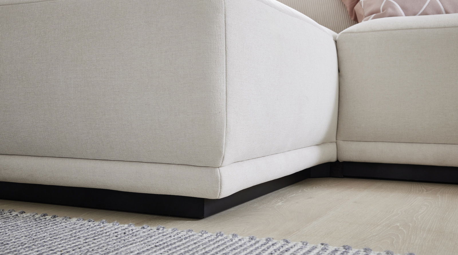 Nahaufnahme einer beigen Polsterrundecke mit schwarzem Sockel auf hellem Holzboden, Perspektive von unten.