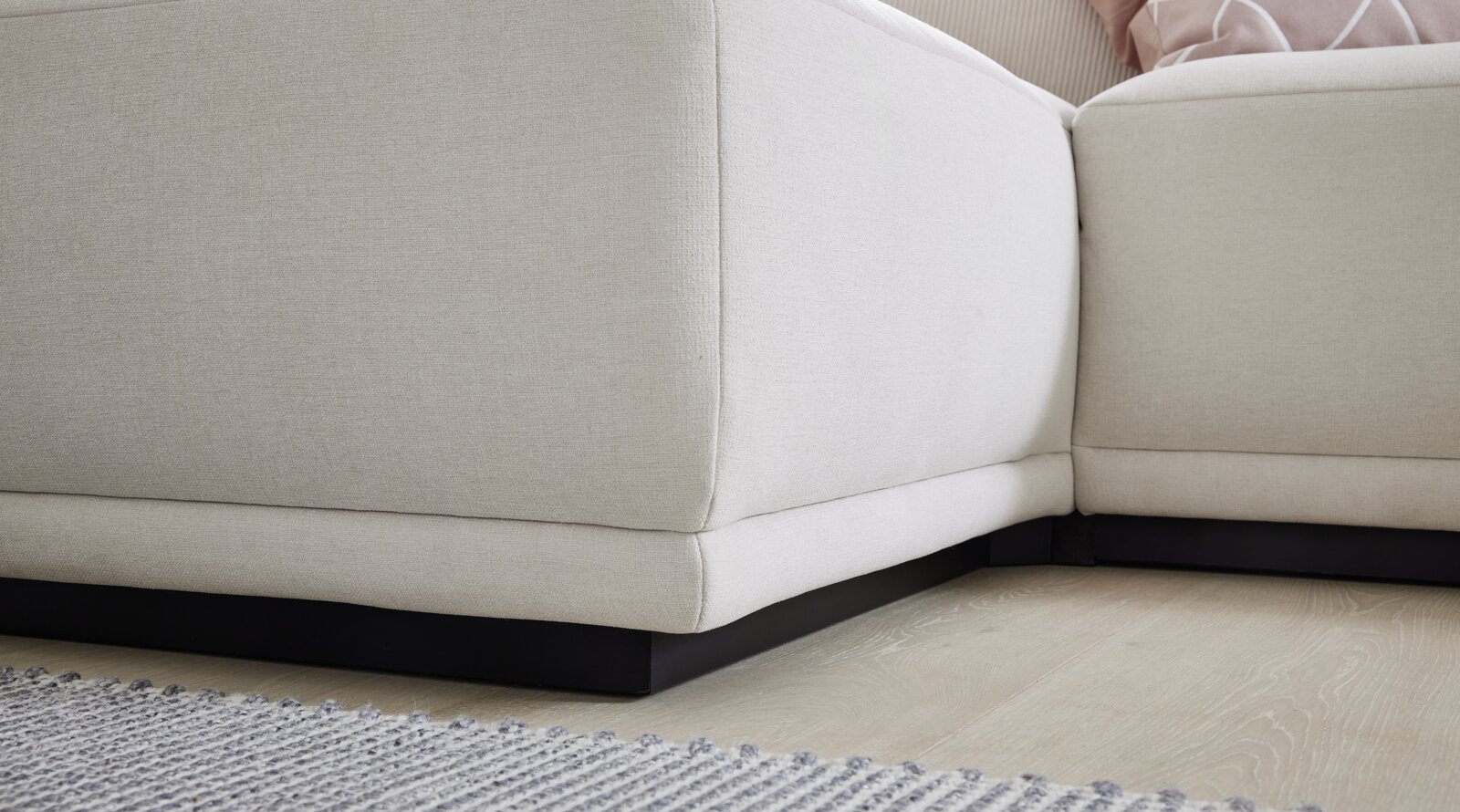 Nahaufnahme einer beigen Polsterrundecke mit schwarzem Sockel auf hellem Holzboden, Perspektive von unten.