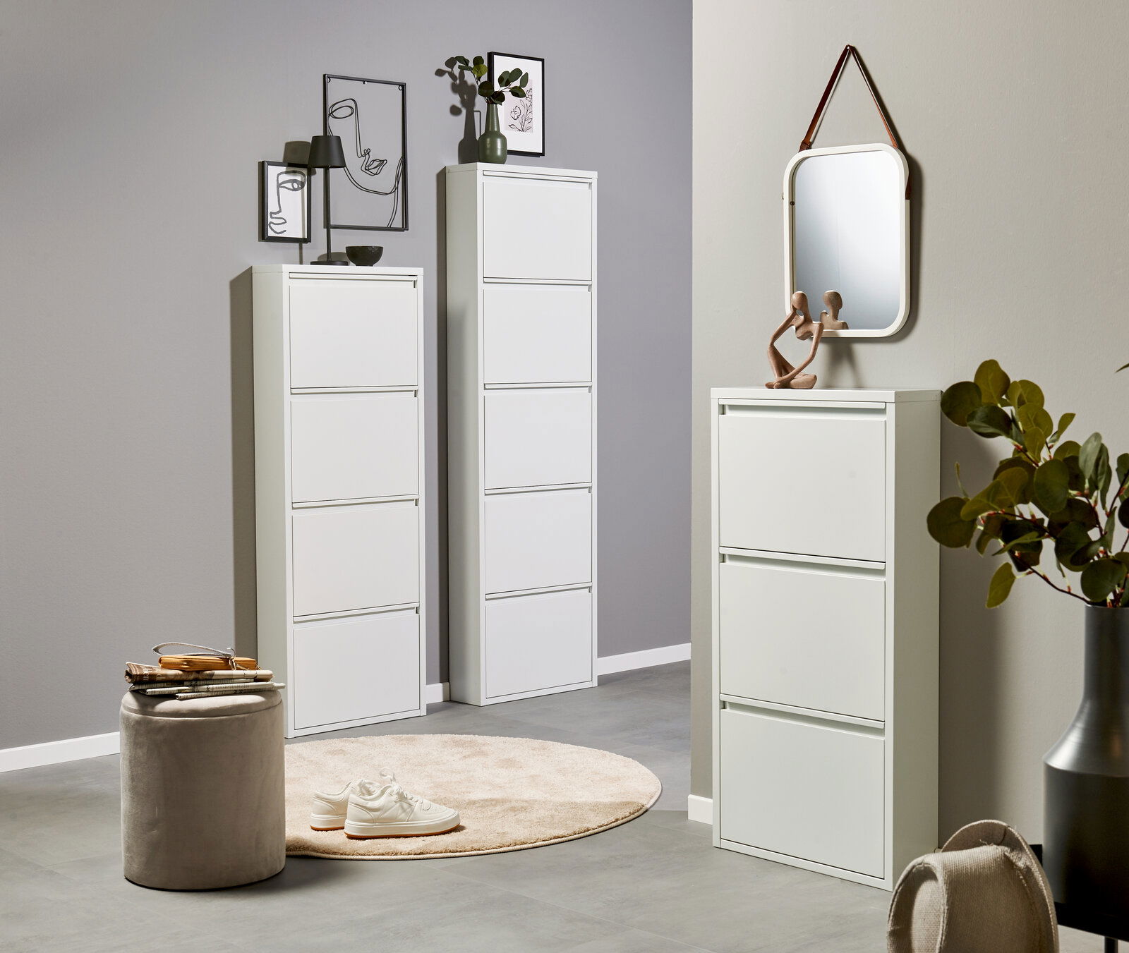 Modernes Wohnambiente mit weißen Schuhschränken/Schuhkippern in verschiedenen Höhen, dekoriert mit Bildern, Lampe und Spiegel; frontale Perspektive auf die Möbel.