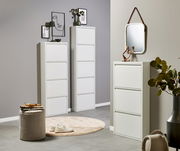 Modernes Wohnambiente mit weißen Schuhschränken/Schuhkippern in verschiedenen Höhen, dekoriert mit Bildern, Lampe und Spiegel; frontale Perspektive auf die Möbel.