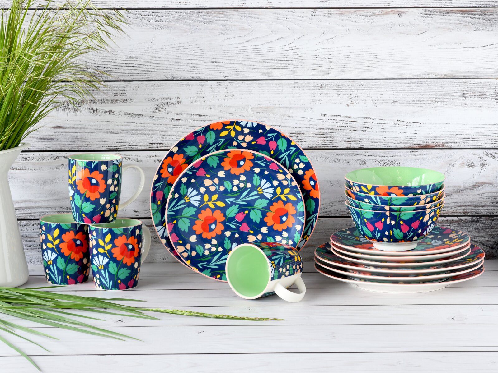 Creatable Kombiservice 16-tlg FOLKLORE Buntes Geschirrset mit floralem Muster in Blau (Teller, Schalen und Tassen) auf weißem Holztisch vor weißer Holzwand, fotografiert in frontaler Perspektive auf Augenhöhe.