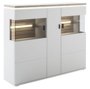 Moderne weiße Highboard-Vitrine mit Holzoptik-Deckplatte, zwei Glasvitrinenfächern mit LED-Beleuchtung und schwarzen Griffen, Ansicht schräg von vorne