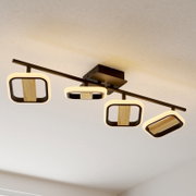 Moderne LED-Deckenleuchte mit vier rechteckigen Lichtmodulen in Schwarz-Metall und Holzoptik auf einer Schiene, warmweiß leuchtend, Perspektive: leicht von unten schräg aufgenommen