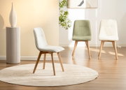 Drei moderne Stühle mit Holzbeinen, einer in der Mitte im Vordergrund in Weiß, die anderen zwei im Hintergrund in Grün und Weiß, auf einem hellen Teppich in einem stilvoll eingerichteten Raum.