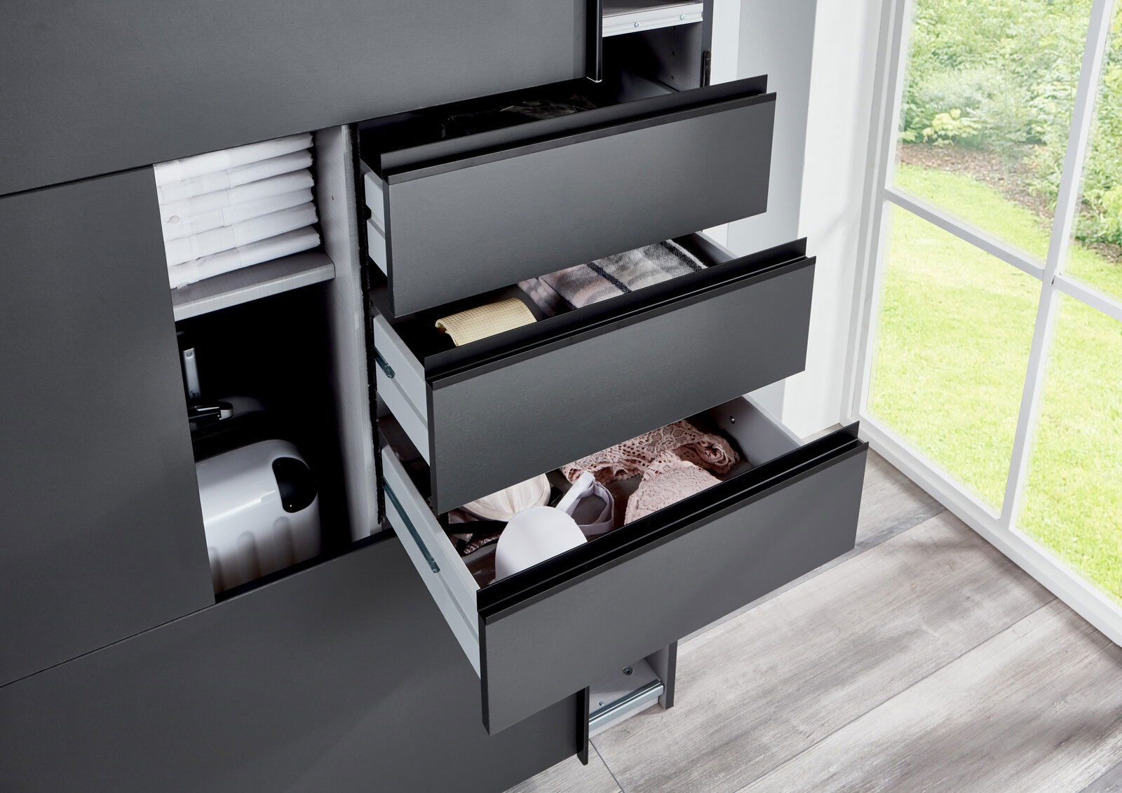 Nahaufnahme eines Schwebetürenschranks mit geöffneten Schubladen, gefüllt mit Kleidung und Accessoires, von der Seite betrachtet.