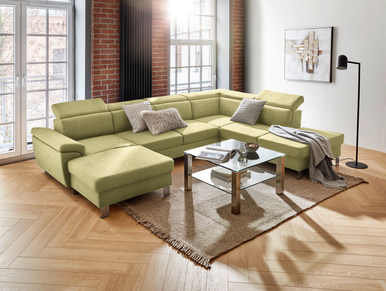 Grüne Rundecke mit modernem Design in einem Wohnzimmer, fotografiert aus einer leicht erhöhten Perspektive. Die Couch ist mit Kissen dekoriert und steht auf einem Teppich neben einem Glastisch.