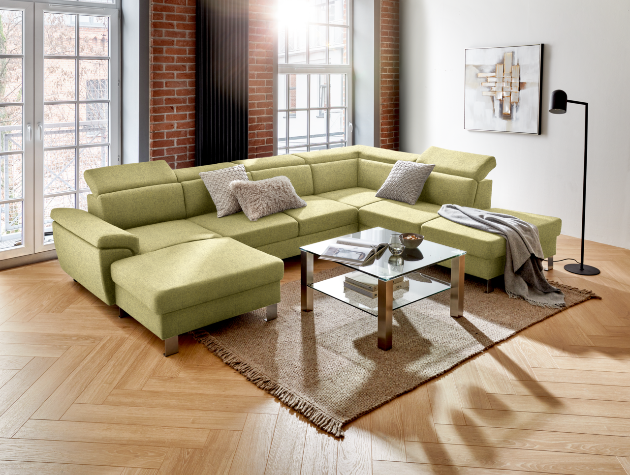 Grüne Rundecke mit modernem Design in einem Wohnzimmer, fotografiert aus einer leicht erhöhten Perspektive. Die Couch ist mit Kissen dekoriert und steht auf einem Teppich neben einem Glastisch.