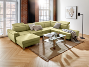 Grüne Rundecke mit modernem Design in einem Wohnzimmer, fotografiert aus einer leicht erhöhten Perspektive. Die Couch ist mit Kissen dekoriert und steht auf einem Teppich neben einem Glastisch.