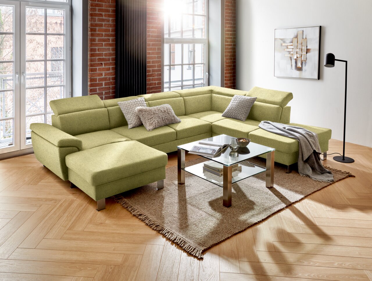 Groene hoekbank met een modern ontwerp in een woonkamer, gefotografeerd vanuit een iets hoger standpunt. De bank is versierd met kussens en staat op een tapijt naast een glazen tafel.