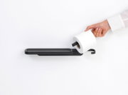 Moderner Toilettenpapierhalter mit Ablage in seitlicher Perspektive, Hand legt eine Toilettenpapierrolle auf den Halter.