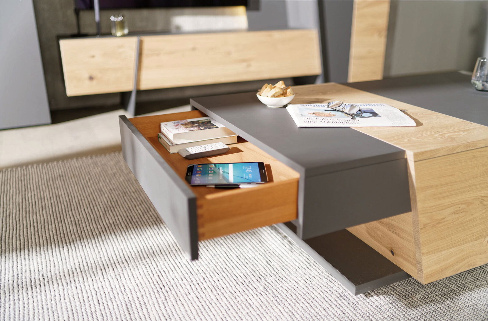 Moderner Couchtisch mit Holz- und Grauelementen, Schublade geöffnet, von schräg oben fotografiert.
