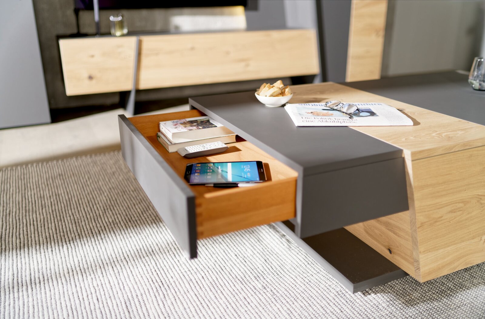 Moderner Couchtisch mit Holz- und Grauelementen, Schublade geöffnet, von schräg oben fotografiert.