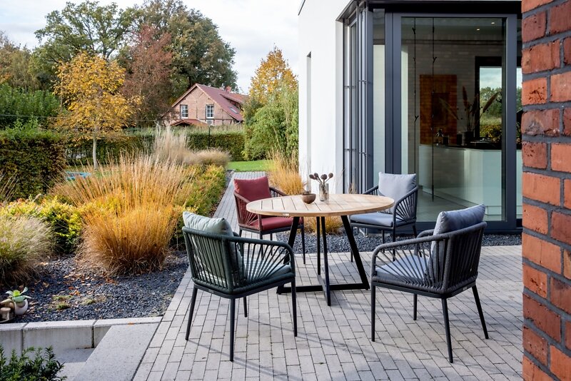 Een moderne designfauteuil op een terras, omgeven door een herfstachtig tuinlandschap, gezien vanuit een schuin vooraanzicht.