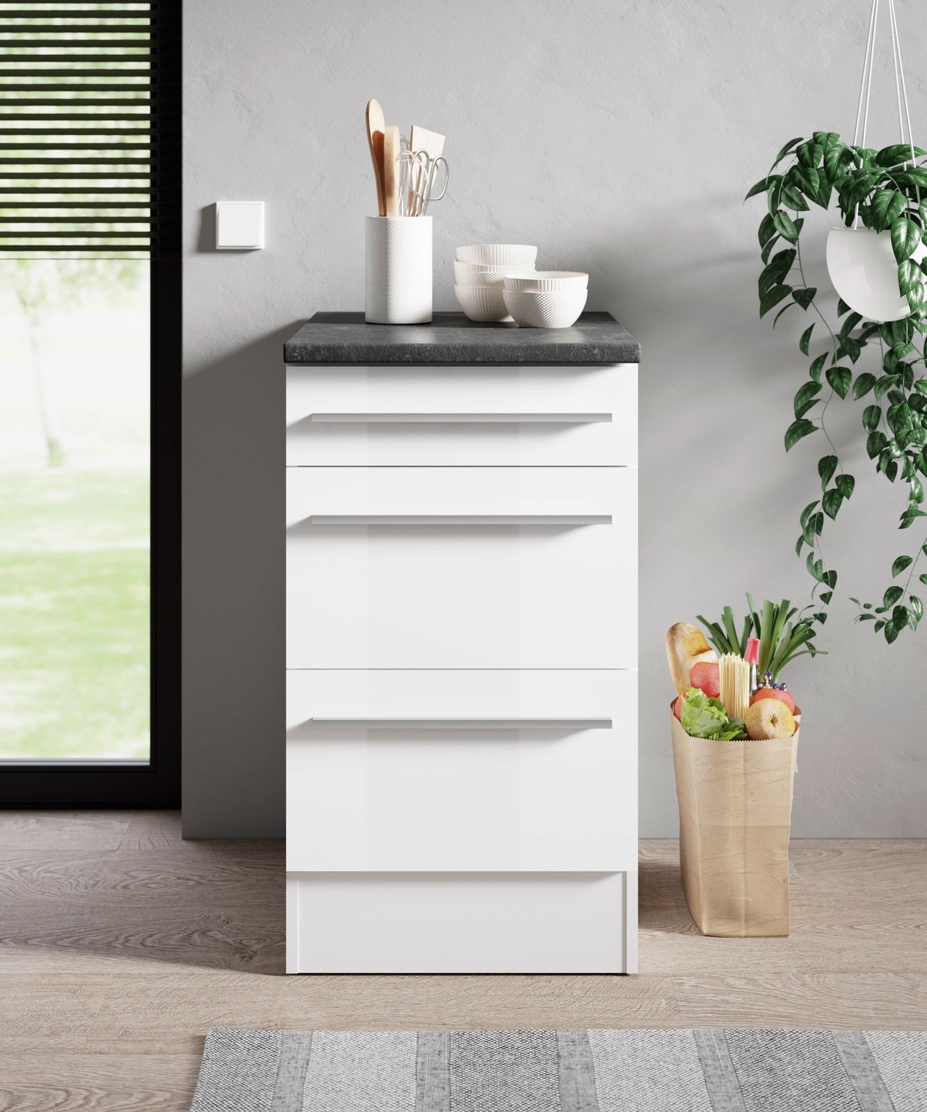 Moderner weißer Unterschrank mit drei Schubladen, schwarze Arbeitsplatte, Küchenutensilien und Schalen darauf, seitliche Perspektive.