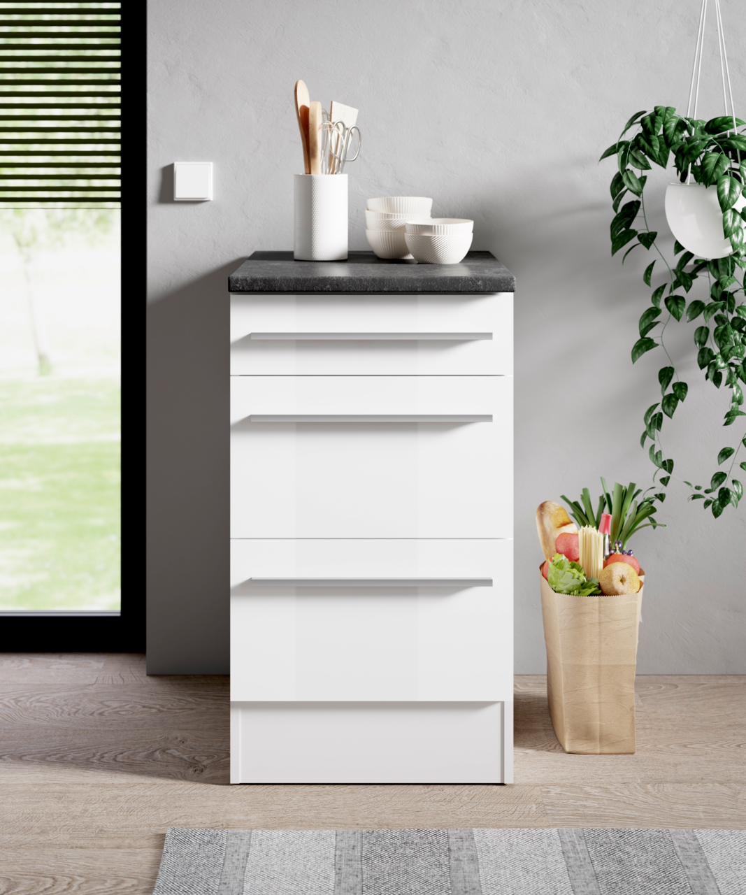 Moderner weißer Unterschrank mit drei Schubladen, schwarze Arbeitsplatte, Küchenutensilien und Schalen darauf, seitliche Perspektive.