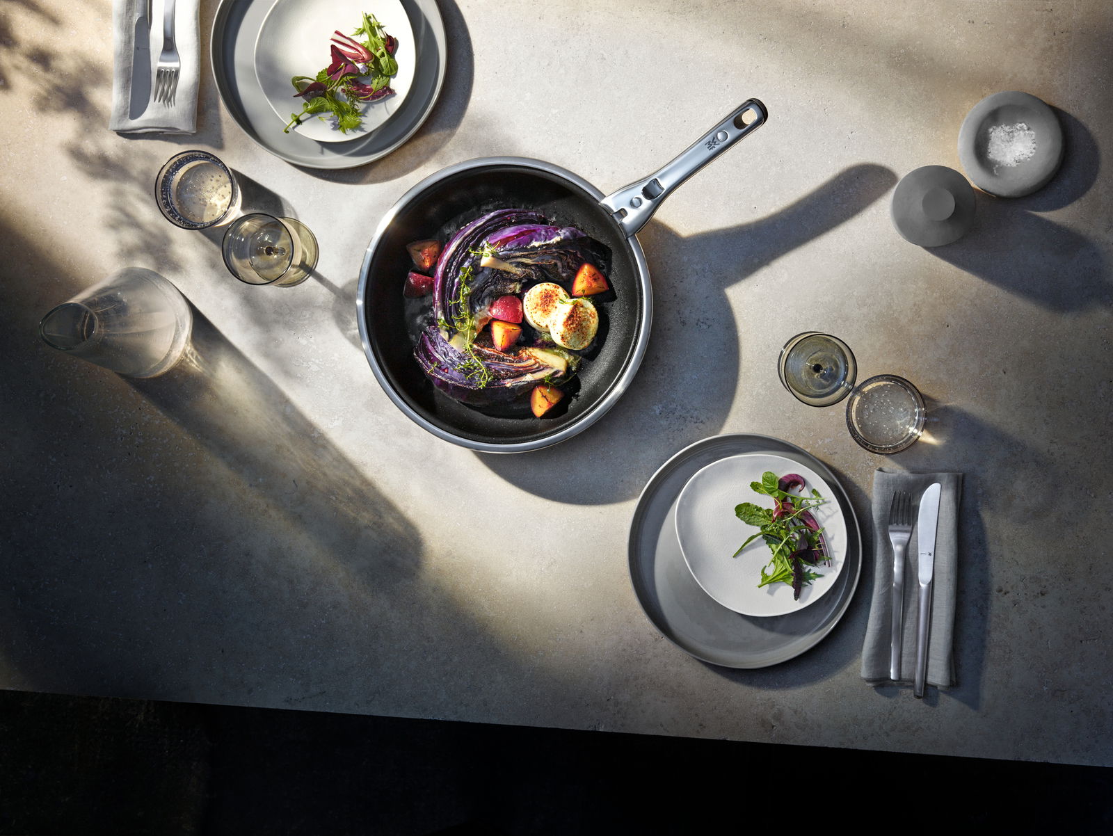 Top-Down-Ansicht eines gedeckten Tisches mit einer Pfanne aus dem Topfset Click & Serve, gefüllt mit Gemüse und dekoriert mit frischen Zutaten.