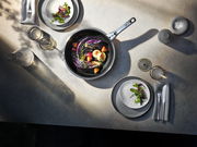 Top-Down-Ansicht eines gedeckten Tisches mit einer Pfanne aus dem Topfset Click & Serve, gefüllt mit Gemüse und dekoriert mit frischen Zutaten.