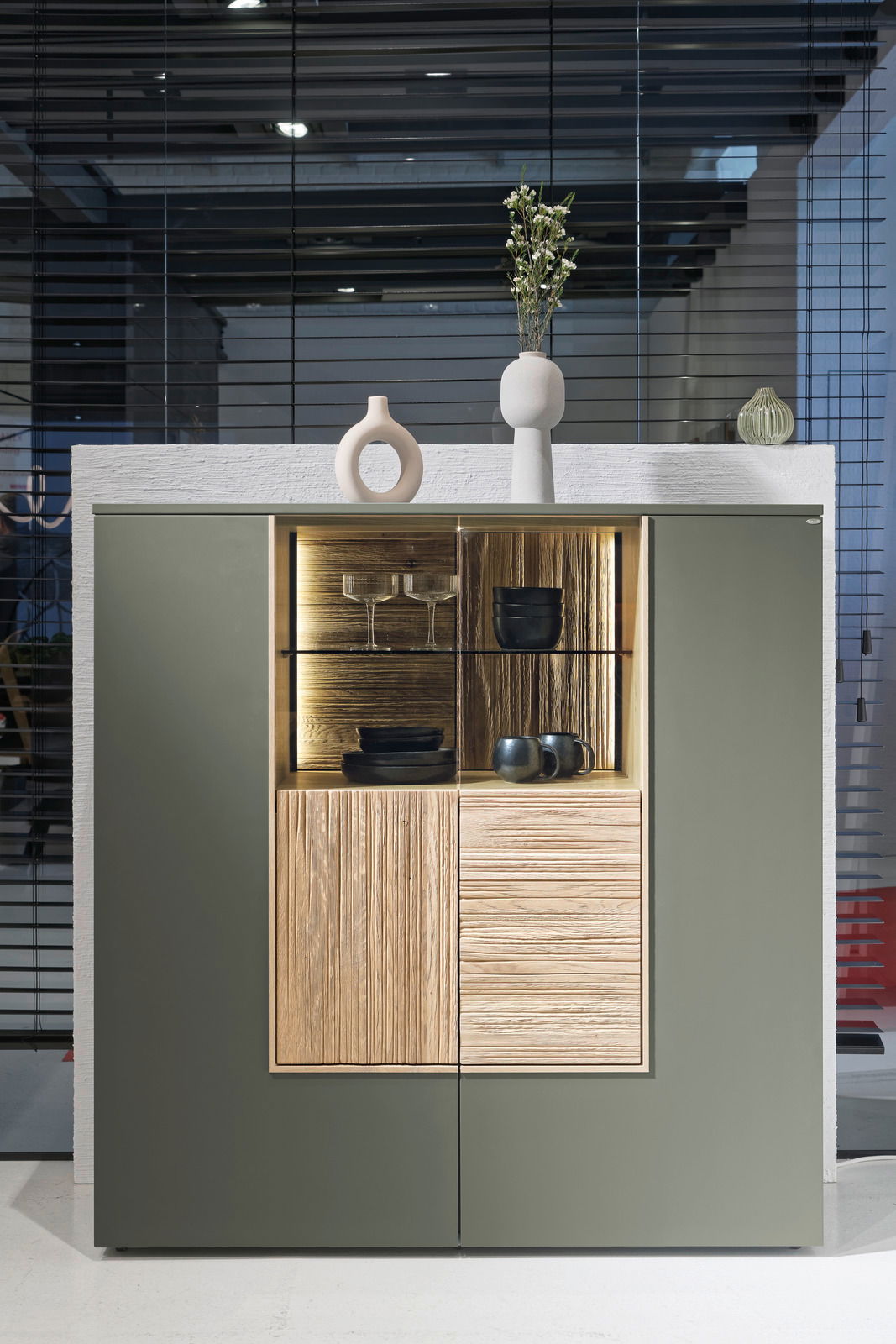 Frontale Ansicht eines modernen Highboards mit grünen Türen, einem offenen Fach mit Beleuchtung und dekorativen Vasen oben.