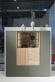 Frontale Ansicht eines modernen Highboards mit grünen Türen, einem offenen Fach mit Beleuchtung und dekorativen Vasen oben.