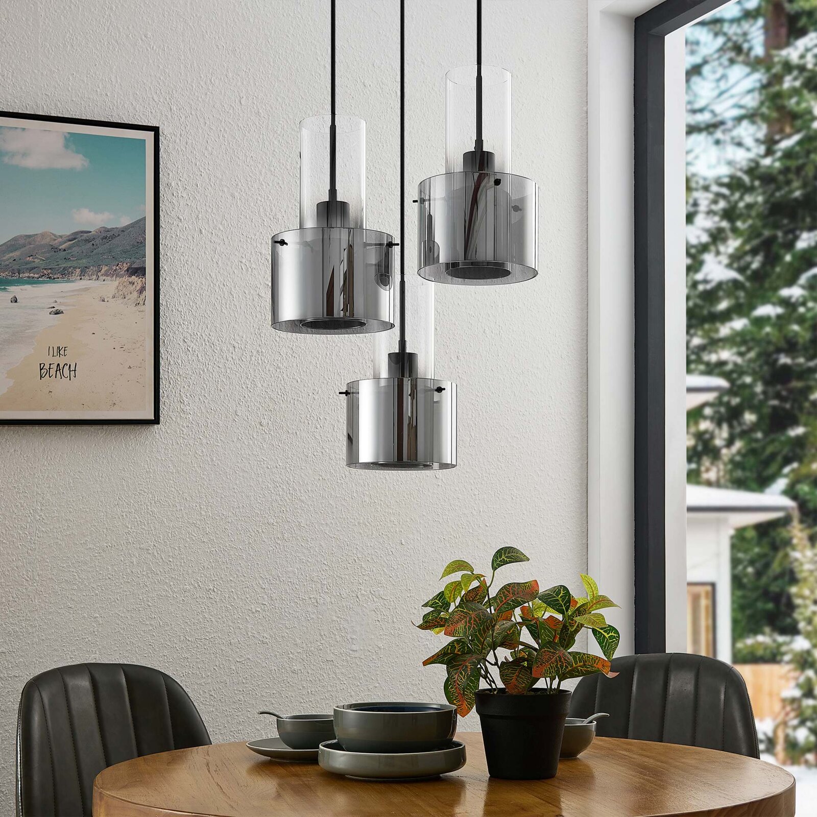 Moderne Hängeleuchte mit drei zylindrischen, rauchgrauen Glasschirmen, hängend über einem Esstisch in einem stilvoll eingerichteten Raum, seitliche Perspektive.