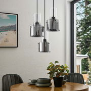 Moderne Hängeleuchte mit drei zylindrischen, rauchgrauen Glasschirmen, hängend über einem Esstisch in einem stilvoll eingerichteten Raum, seitliche Perspektive.