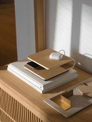 Kabelloses Ladegerät aus Holz in seitlicher Perspektive auf einem Tisch, mit einem Smartphone und einem weißen Ladecase darauf.