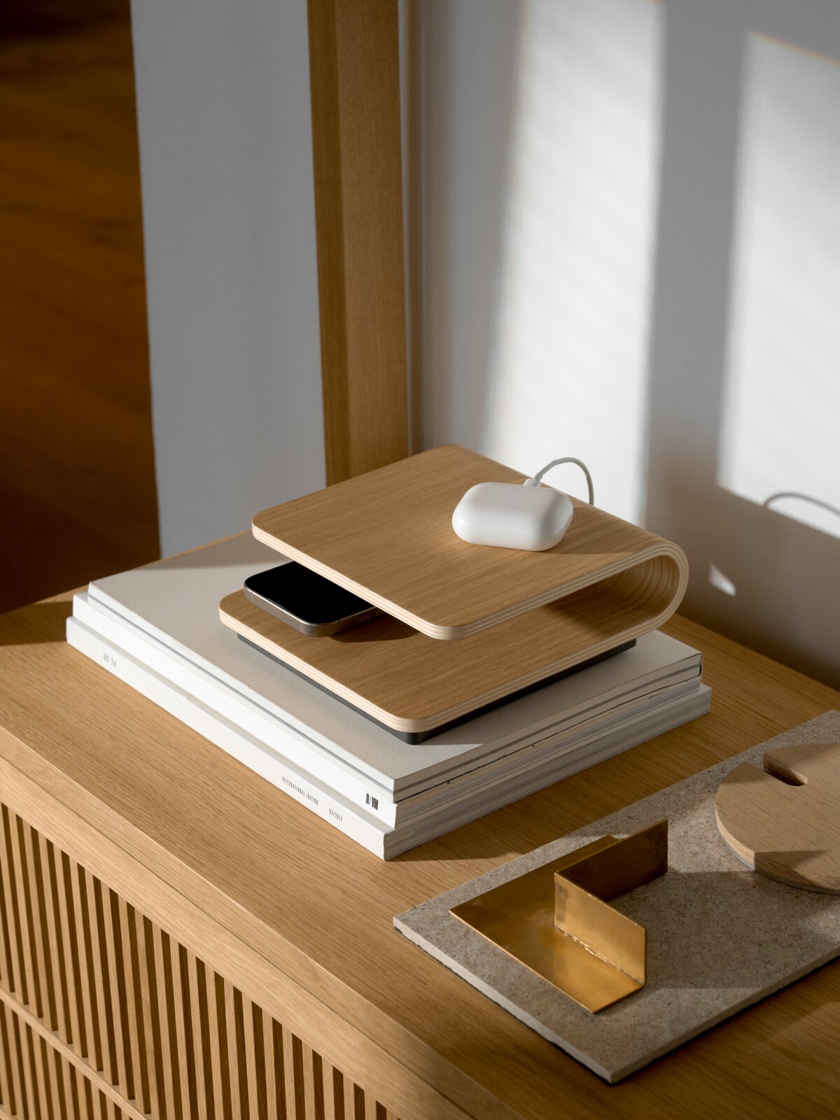 Stelton Kabelloses Ladegerät RO Kabelloses Ladegerät aus Holz in seitlicher Perspektive auf einem Tisch, mit einem Smartphone und einem weißen Ladecase darauf.