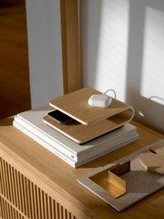 Kabelloses Ladegerät aus Holz in seitlicher Perspektive auf einem Tisch, mit einem Smartphone und einem weißen Ladecase darauf.